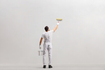 Rear view shot of a painter holding a bucket and painting a wall