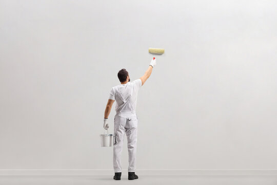 Rear view shot of a painter holding a bucket and painting a wall