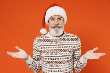 Old shocked bearded Santa Claus man 50s wears Christmas hat sweater posing shrugging shoulders look puzzled have no idea nothing to say standing questioned isolated on plain orange background studio.