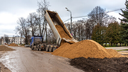 A large dump truck dumps sand on the street to repair the road surface.