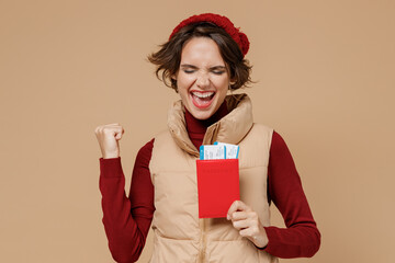 Traveler tourist woman in vest red beret hold passport tickets do winner gesture isolated on plain...