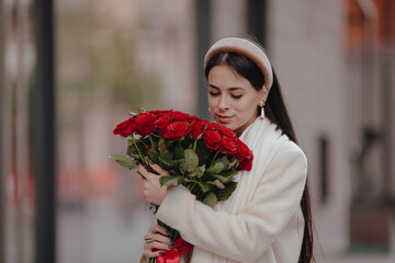 Fototapeta premium Happy woman carries and sniffs flowers walking around the city