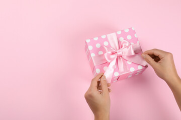 Female hands and gift box with bow on pink background