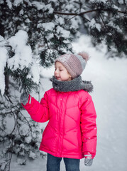 Little girl in a bright jacket plays in the winter forest