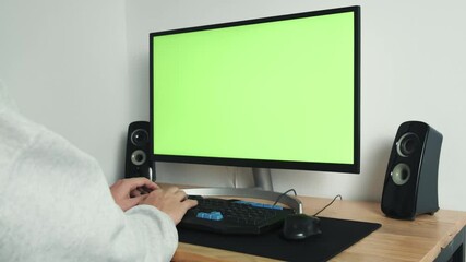 A close-up shot from behind the shoulder of a guy who works at home on a computer with a green screen and uses a mouse and keyboard. Green chromakey screen. High quality 4k footage
