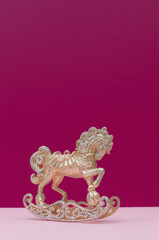 Golden and silver Christmas toy horse decoration on a pastel pink and dark mauve background. Copy space.