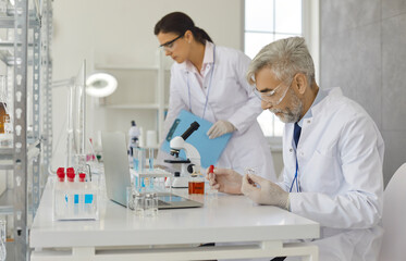 Senior male scientist doing experiments in laboratory by pipetting samples of cell culture medium....