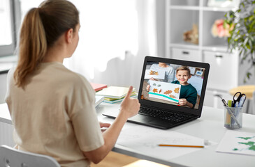 education, online school and distant learning concept - female art teacher having video call with student boy holding autumn picture on laptop computer screen and showing him thumbs up at home