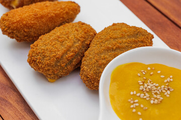Fried croquettes with yellow sauce on white plate. Side view on wooden background.