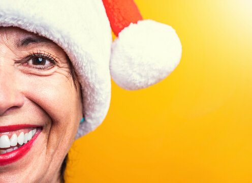 Senior Woman Portrait Wearing Santa Claus Hat On A Yellow Background - Mature Female Celebrating Christmas - Festive People Enjoying Xmas Holidays