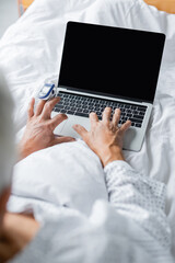 Obraz na płótnie Canvas Blurred patient with pulse oximeter using laptop with blank screen on bed