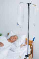 Intravenous therapy stand near blurred patient on bed in hospital
