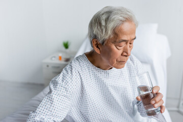 Elderly asian patient holding glass of water in hospital ward