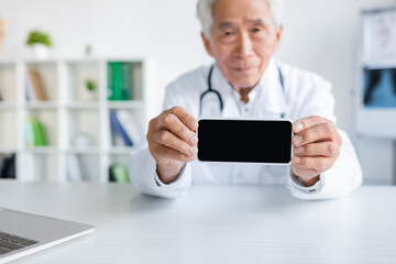 Smartphone with blank screen in hands of blurred asian doctor in hospital