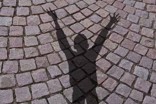 blurred black shadow of a child with raised hands in a pleading gesture against background of old stone tile paving, the concept of domestic violence, a victim of abuse