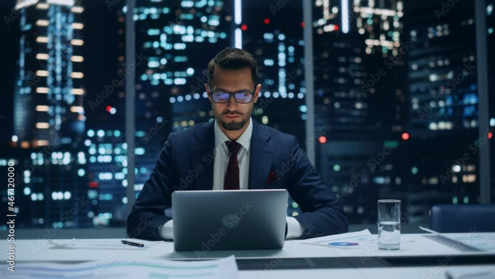 Poster successful handsome businessman working on laptop computer in big city office late in the evening. f