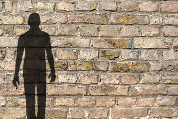 blurred black shadow of man on old brick wall background, concept of undercover killer, criminal in...