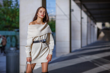 Fashion blogger outfit details. Fashionable woman wearing a white oversized sweater dress, holding a black trendy handbag. Detail of a perfect fall fashion outfit.