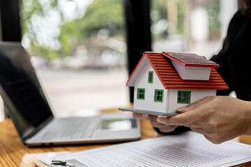 Fototapeta premium Model of a house placed on a woman's hand, a housing salesman in the project, a portrait holding a house project to the front similar to delivering homes to customers. Real estate trading ideas.