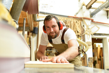 carpenter works in a joinery - workshop for woodworking and sawing - obrazy, fototapety, plakaty