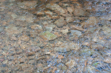 Sun glare on surface water and smooth stones at bottom stream, background. Transparent water in river with rocky bottom, fast flow
