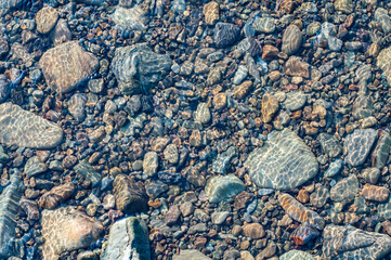 Sun glare on surface water and smooth stones at bottom stream, background. Transparent water in...