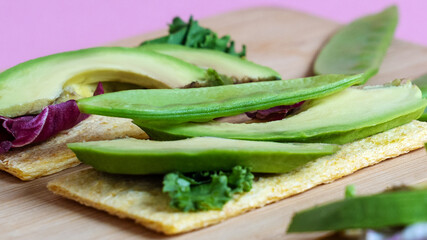 Horizontal closeup view of vegetarian toasts with avocado, green pea and salad, on lilac pink background. Healthy food concept. Copy space.