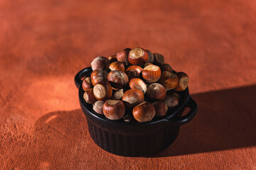 whole hazelnuts in a dark cup on a colored background