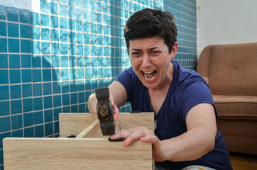 A dark-haired woman screams in pain, hits herself on the finger with a hammer, trying to assemble furniture on her own at home. Furniture assembly, DIY