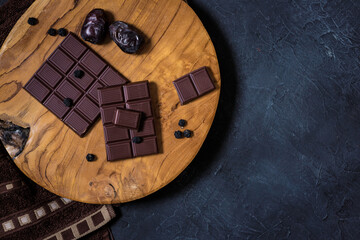 Top view of dark vegan chocolate on a wooden cutting board with dates on painted background. Moody dark atmosphere low key flat lay. Copy space included 