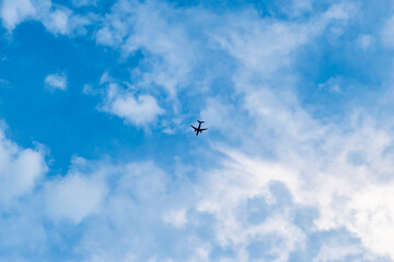 Dark silhouette of a flying passenger plane against a blue sky with clouds