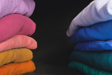 Stacks of multicolored fabrics in cool and warm colors are compared next to each other. Background with folded clothes with blank space for information. T-shirts of different colors