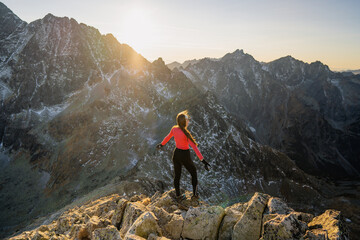 Back view of adventure woman near on rock. Joyful woman travel mountains. Hiker meets the sunset....