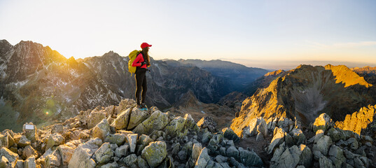 Lady hiker with backpack standing on top of the mountain and enjoying valley view. Hiker meets the sunset. Adventure concept. 
