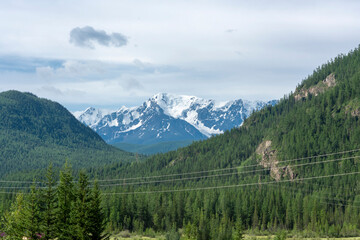 peaks of mountains against the sky with white clouds. Summer day . High snowy peaks in the distance