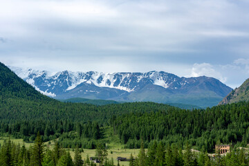 peaks of mountains against the sky with white clouds. Summer day . High snowy peaks in the distance