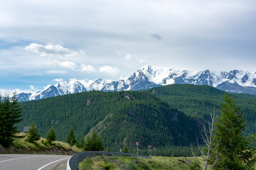 peaks of mountains against the sky with white clouds. Summer day . High snowy peaks in the distance. Mountain asphalt road
