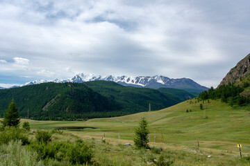 peaks of mountains against the sky with white clouds. Summer day . High snowy peaks in the distance