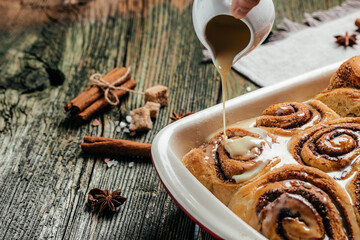 Traditional Cinnamon Rolls with white cream sauce on wooden background. banner, menu, recipe place for text, top view