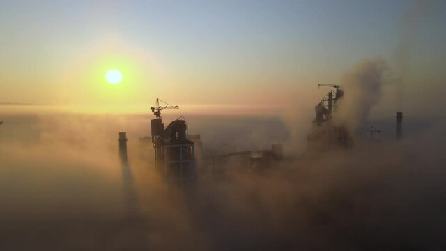 Aerial view of cement factory with high concrete plant structure and tower crane at industrial production site on foggy morning. Manufacture and global industry concept