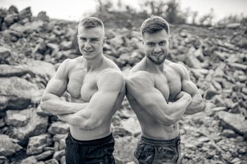 Brutal strong bodybuilders pumping up muscles while posing. Bodybuilding and outdoor sports concept. Two male athletes