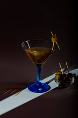 Still-life. Beautiful martini glass and light olives on a dark background with creative lighting
