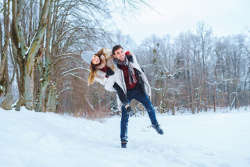 Fototapeta na wymiar Happy young man carry his smiling pretty woman on his back at winter park. Boyfriend giving piggyback ride on shoulder to his girlfriend in winter holiday.