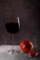 A simple still life. A beautiful glass of red wine, a plate with pomegranate seeds and a peach on a dark background with creative lighting