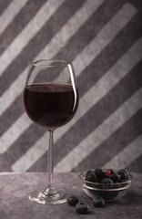 a simple still life. a beautiful glass with red wine, a glass plate with blue berries on a dark background with creative lighting