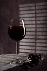 A simple still life. A beautiful glass with red wine and a plate with blue berries on a dark background with creative lighting