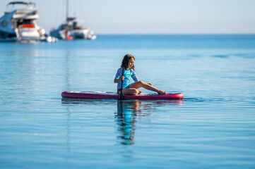 Child girl is riding SUP stand up paddle on vacation.