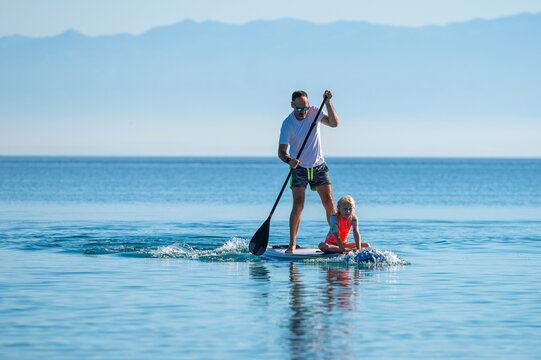 Father and daughter riding SUP stand up paddle on vacation.