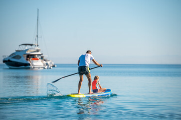 Father and daughter riding SUP stand up paddle on vacation.