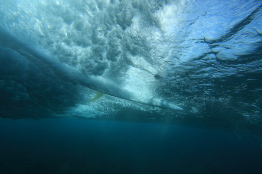 Surfer Riding A Surfboard On A Wave Photographed From Underwater With The Sun Behind Him